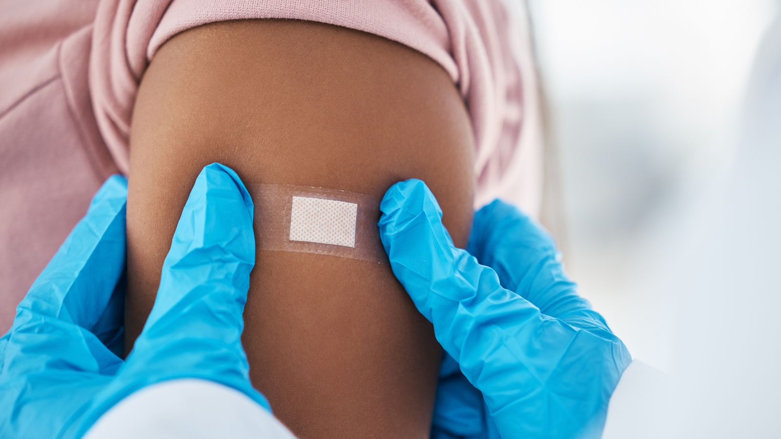 Doctor with gloves placing a Band-Aid on a patient's arm after a flu shot