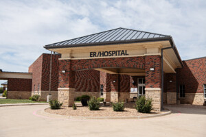 DSC_3162 Front entrance of a brick hospital building with a covered drop-off area and a sign reading “ER/Hospital” above the doorway.